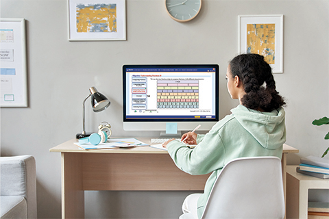 A Girl taking Notes is Sitting on a Chair in Front of a Computer Displaying Educo Learning Center's Online Courses