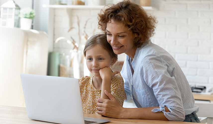 Mother and her Daughter sitting together are looking at a laptop