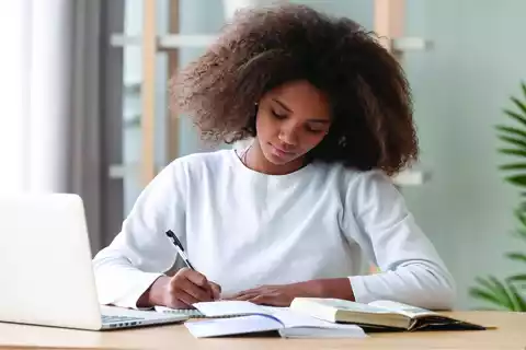 A girl taking notes from math lessons with her books and laptop